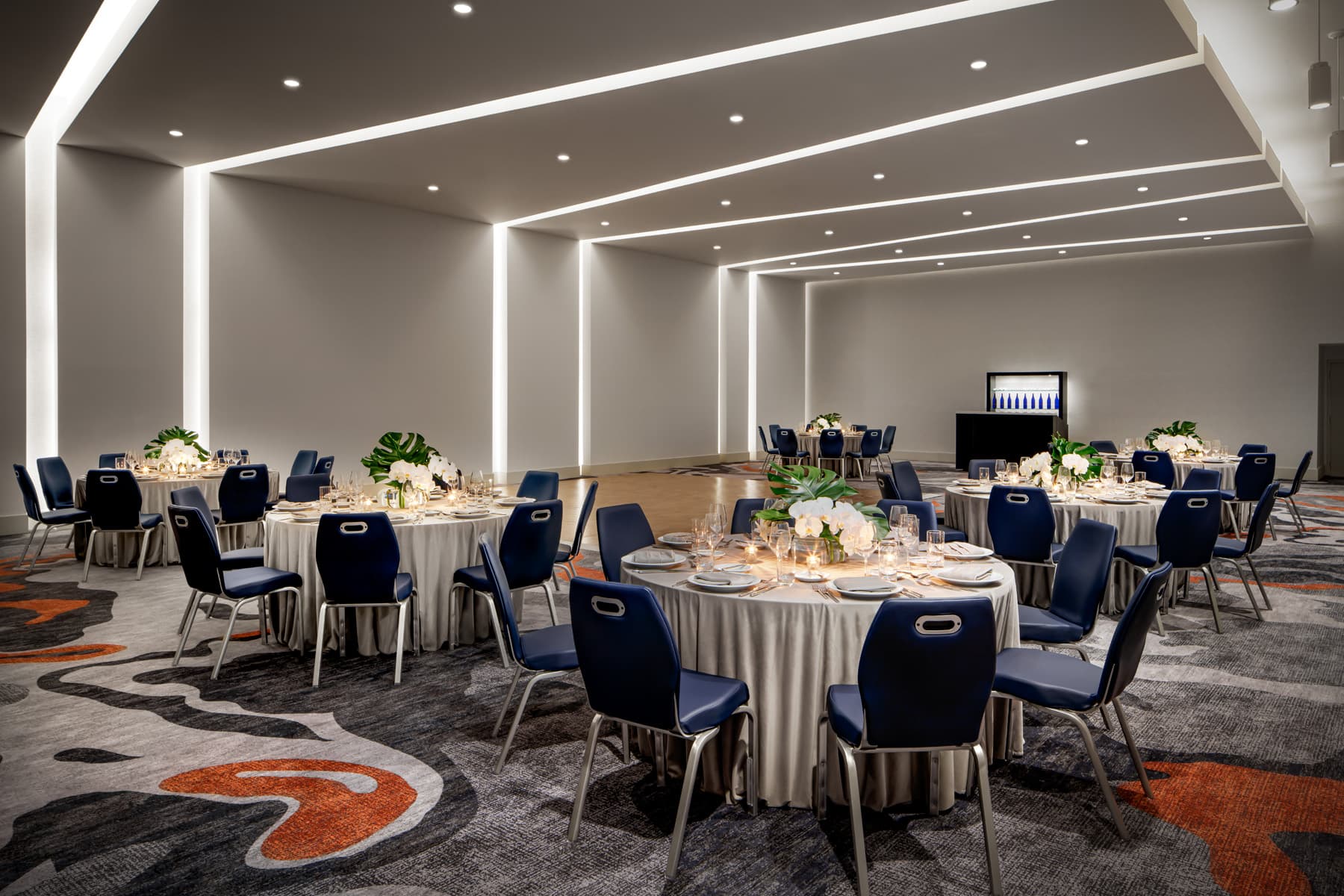 Ballroom set with round tables, navy chairs, floral centerpieces, and warm accent lighting